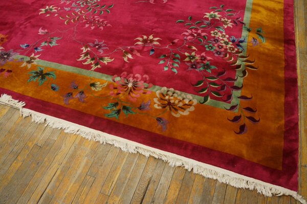 High-pile rug with a magenta field, multi-color florals, an orange border, and white fringe on hardwood flooring.