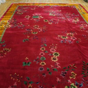 Large, lustrous red rug with scattered multicolor floral patterns and a wide gold border on a wood floor.
