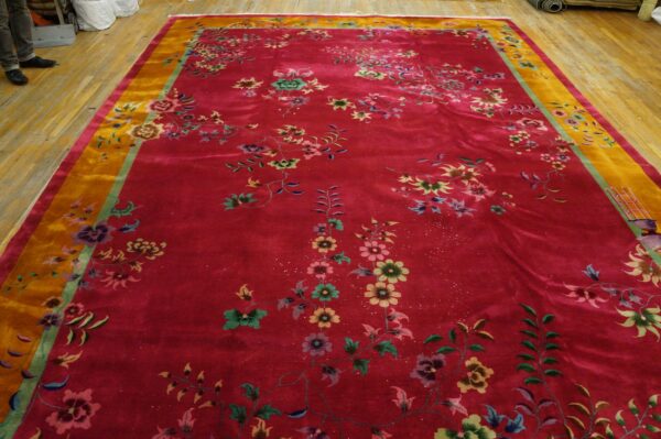 Large, lustrous red rug with scattered multicolor floral patterns and a wide gold border on a wood floor.