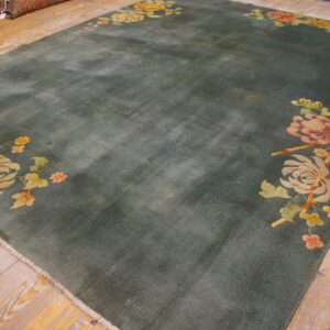 Large teal area rug with corner floral motifs in pink and orange lies on worn wooden planks.