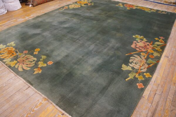 Large teal area rug with corner floral motifs in pink and orange lies on worn wooden planks.