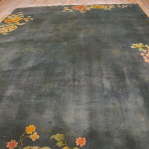 A large dark teal rug featuring colorful pink, yellow, and green floral corner motifs on wood floors.