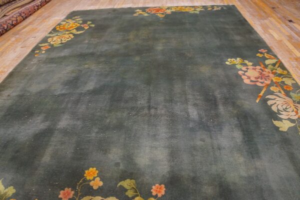 A large dark teal rug featuring colorful pink, yellow, and green floral corner motifs on wood floors.