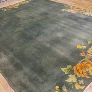 Greenish-blue rug featuring orange, peach, and yellow floral corner designs on rustic light wood planks.