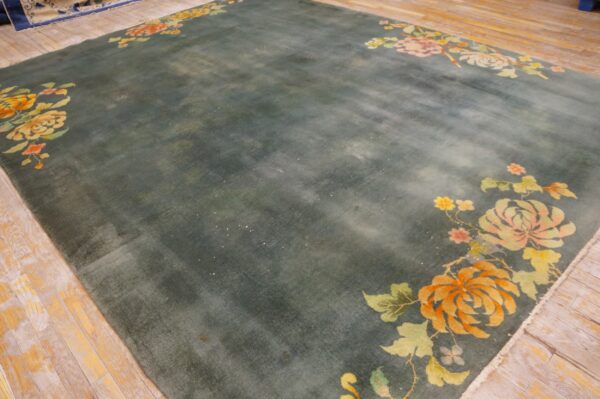 Greenish-blue rug featuring orange, peach, and yellow floral corner designs on rustic light wood planks.
