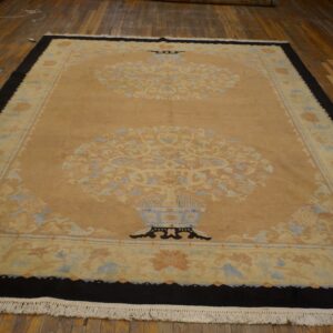 Beige rug featuring two central floral vase designs, a dark border, and fringe on a plank wood floor.