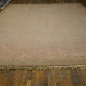 Large blush rug with a subtle floral border and visible fringe rests on dark wood flooring.