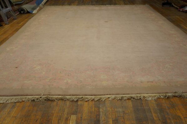 Large blush rug with a subtle floral border and visible fringe rests on dark wood flooring.