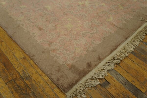 High-pile pink and tan rug with a carved floral pattern rests on rustic yellow wood planks.