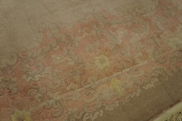 Close-up shows a carved floral pattern in dusty pink, beige, and yellow on a brown high-pile rug.