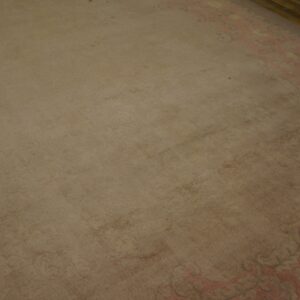 Low-pile beige rug field next to an ornate pink and yellow border on brown wooden flooring.