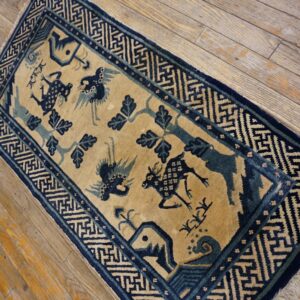 Tan rug with dark blue stylized animals, trees, and geometric borders on worn wood flooring.