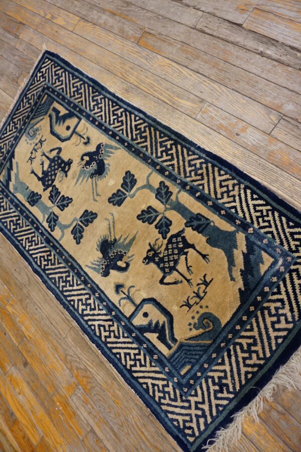 Tan rug with dark blue stylized animals, trees, and geometric borders on worn wood flooring.