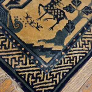 Medium pile rug in tan, dark blue, and teal with stylized animal pattern and fringe over wood planks.