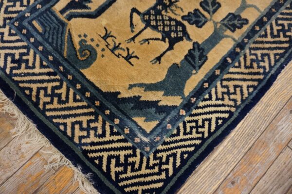 Medium pile rug in tan, dark blue, and teal with stylized animal pattern and fringe over wood planks.
