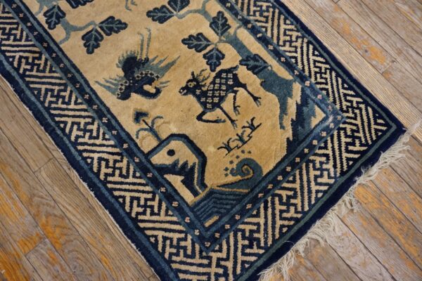 Tan and blue geometric rug with animal motifs rests on distressed, light wood flooring.