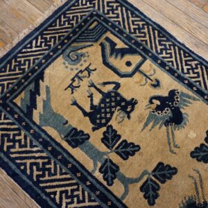 Navy and tan rug with stylized birds and geometric border resting on distressed hardwood planks.