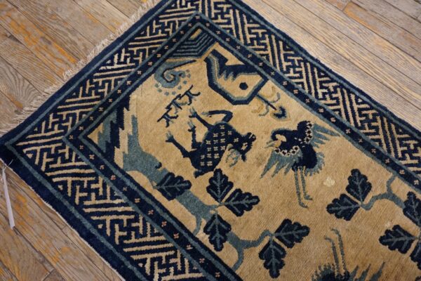 Navy and tan rug with stylized birds and geometric border resting on distressed hardwood planks.