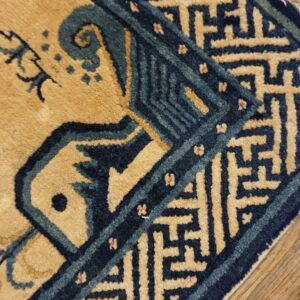 Tan and blue high-contrast rug corner featuring a geometric border rests on distressed wood planks.