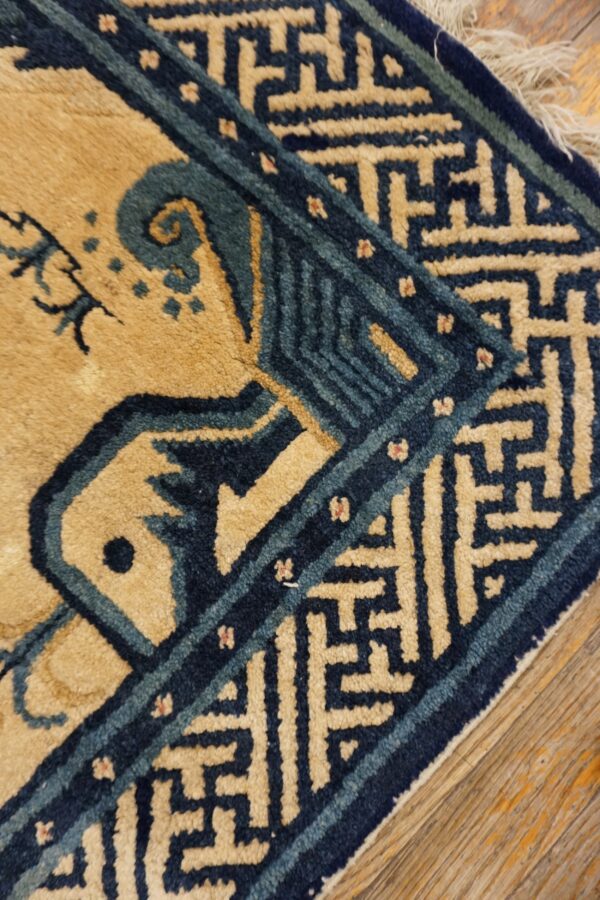 Tan and blue high-contrast rug corner featuring a geometric border rests on distressed wood planks.