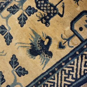 Tan and blue rug featuring stylized birds, leaves, and a geometric border over wood flooring.