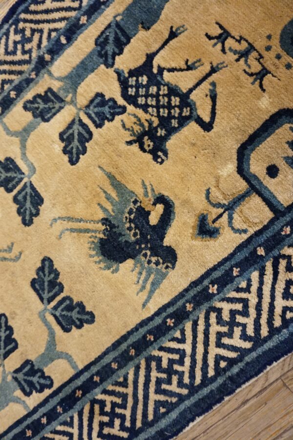 Tan and blue rug featuring stylized birds, leaves, and a geometric border over wood flooring.