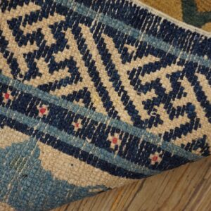 Navy, light blue, and beige geometric pattern on a low-pile rug lying on wood planks.