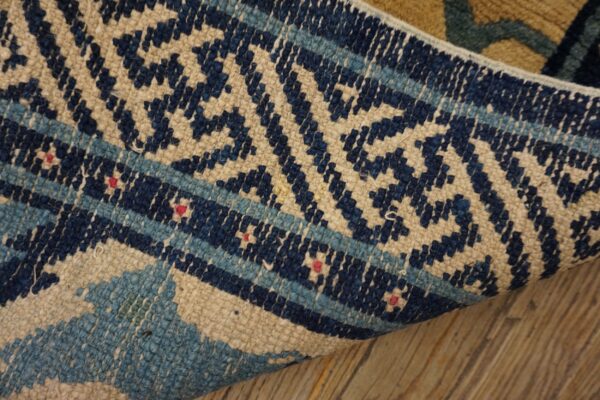 Navy, light blue, and beige geometric pattern on a low-pile rug lying on wood planks.