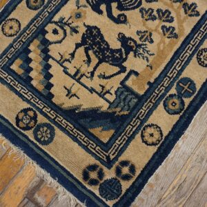 Tan rug with blue geometric and stylized animal patterns rests on worn, yellowed hardwood planks.