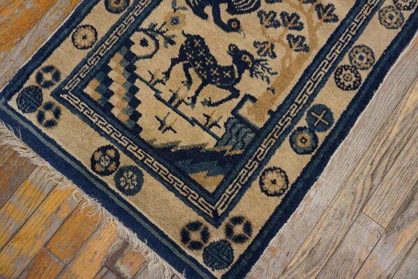 Tan rug with blue geometric and stylized animal patterns rests on worn, yellowed hardwood planks.