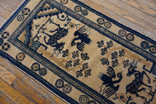 A low pile tan rug with navy blue deer and bird patterns lies diagonally across rustic wooden flooring.