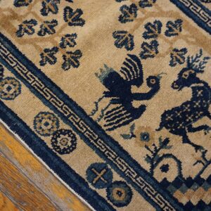 Low-pile beige rug with a navy figurative animal pattern and geometric borders rests on distressed wood planks.