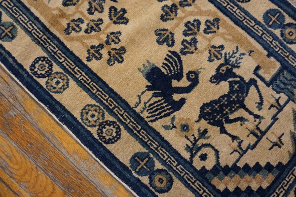 Low-pile beige rug with a navy figurative animal pattern and geometric borders rests on distressed wood planks.