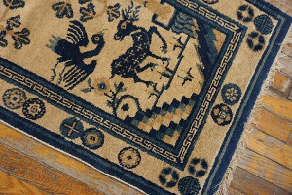 Tan rug with dark blue animal figures, patterned borders, and fringe rests on distressed wood flooring.
