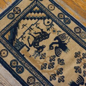 Tan rug with navy border and stylized bird motifs rests on distressed hardwood planks.
