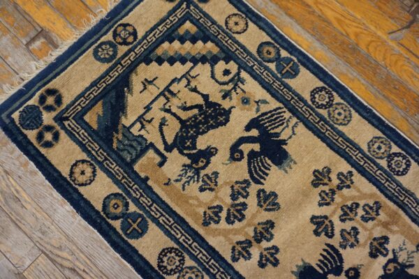 Tan rug with navy border and stylized bird motifs rests on distressed hardwood planks.