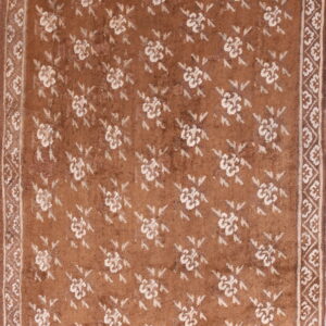 Brown rug with a low pile features repeated white floral medallions and patterned white borders.