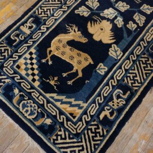 Dark blue rug with a tan deer motif and geometric borders on distressed wood planks.