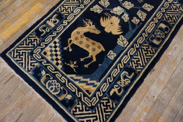 Dark blue rug with a tan deer motif and geometric borders on distressed wood planks.