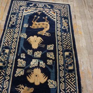 Navy blue rug runner with beige animal and vine patterns laid over pale, distressed wood planks.