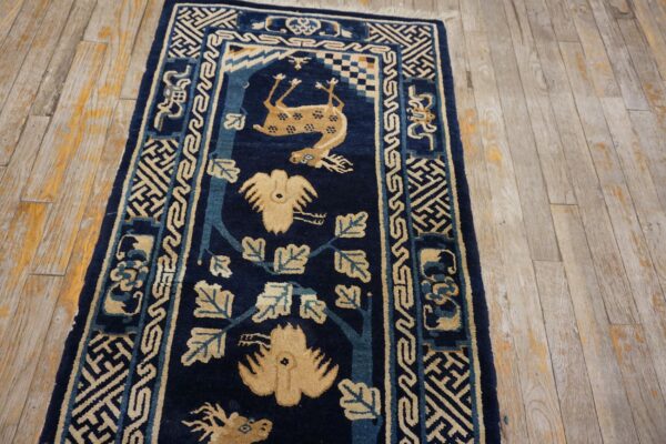 Navy blue rug runner with beige animal and vine patterns laid over pale, distressed wood planks.