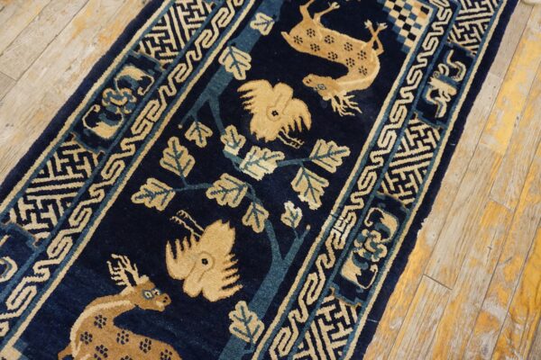 Navy blue runner with beige deer and stylized trees, framed by geometric borders on worn wood planks.