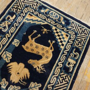 Dark blue and tan rug with animal motifs and geometric borders rests on distressed wood flooring.