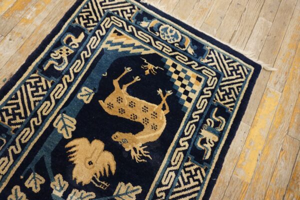 Dark blue and tan rug with animal motifs and geometric borders rests on distressed wood flooring.