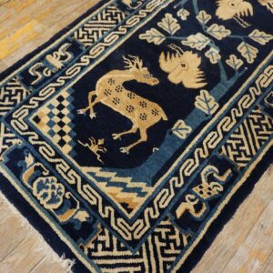 Navy blue rug with tan spotted deer, bird, and stylized foliage placed on distressed light wood floors.