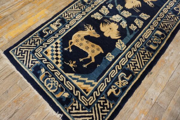 Navy blue rug with tan spotted deer, bird, and stylized foliage placed on distressed light wood floors.