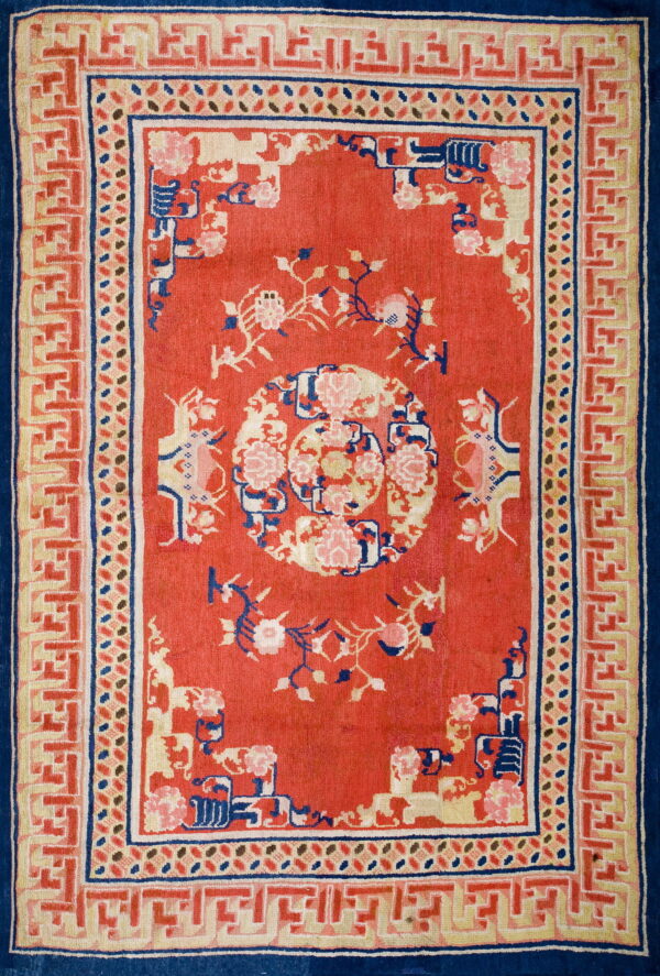 Red rug with a central medallion, peonies, and a complex blue and cream key-pattern border.