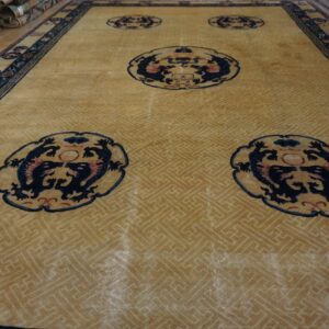 High-pile gold rug with navy blue dragon medallions, a fret pattern field, and detailed border.
