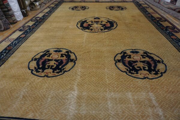 High-pile gold rug with navy blue dragon medallions, a fret pattern field, and detailed border.