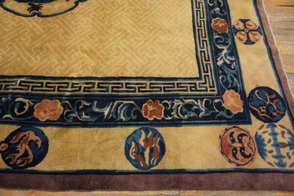 Gold and navy rug corner featuring florals and greek key borders rests on distressed wood flooring.